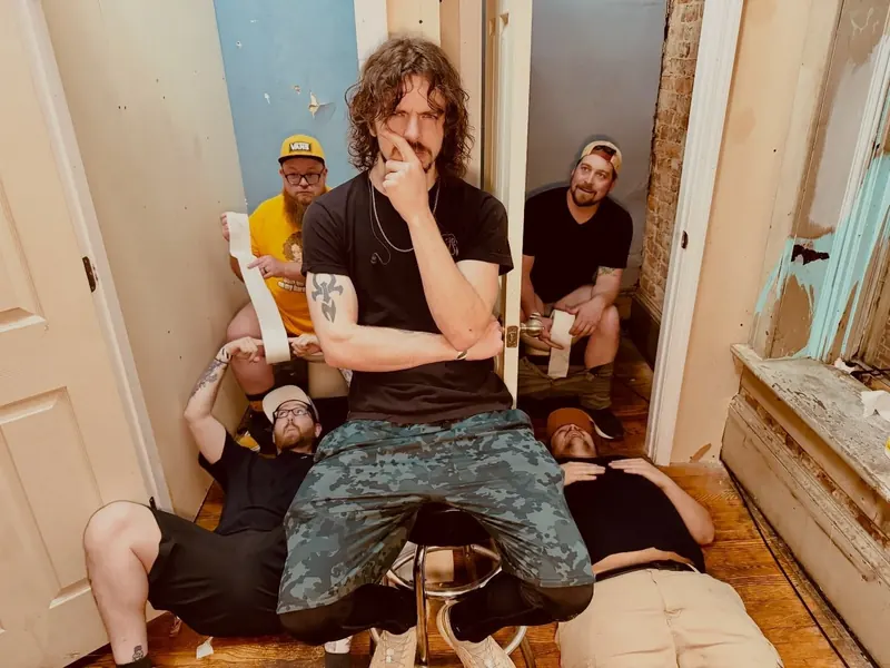 Band member seated backstage while the rest of the band sprawls on the floor