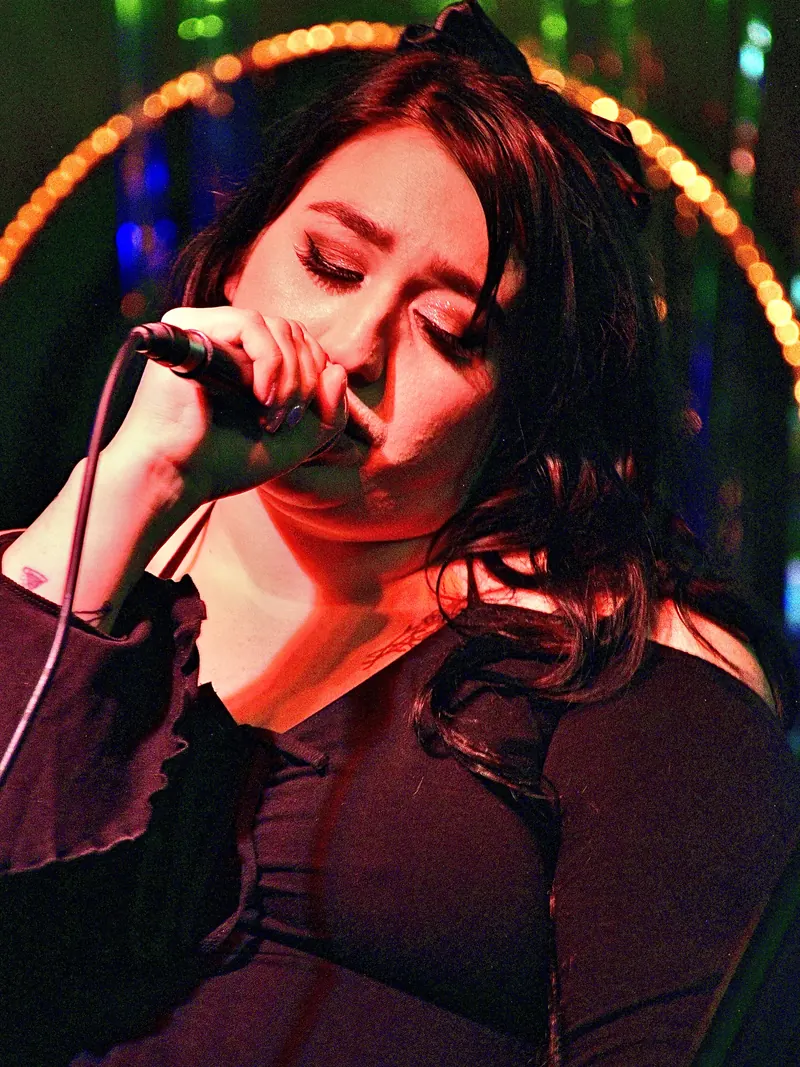 Singer with eyes closed at the microphone, a ring of stage bulbs behind