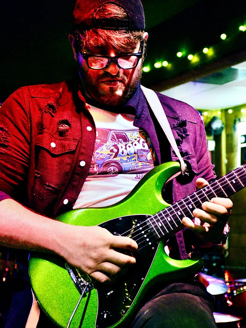 Guitarist in a red jacket playing a green guitar