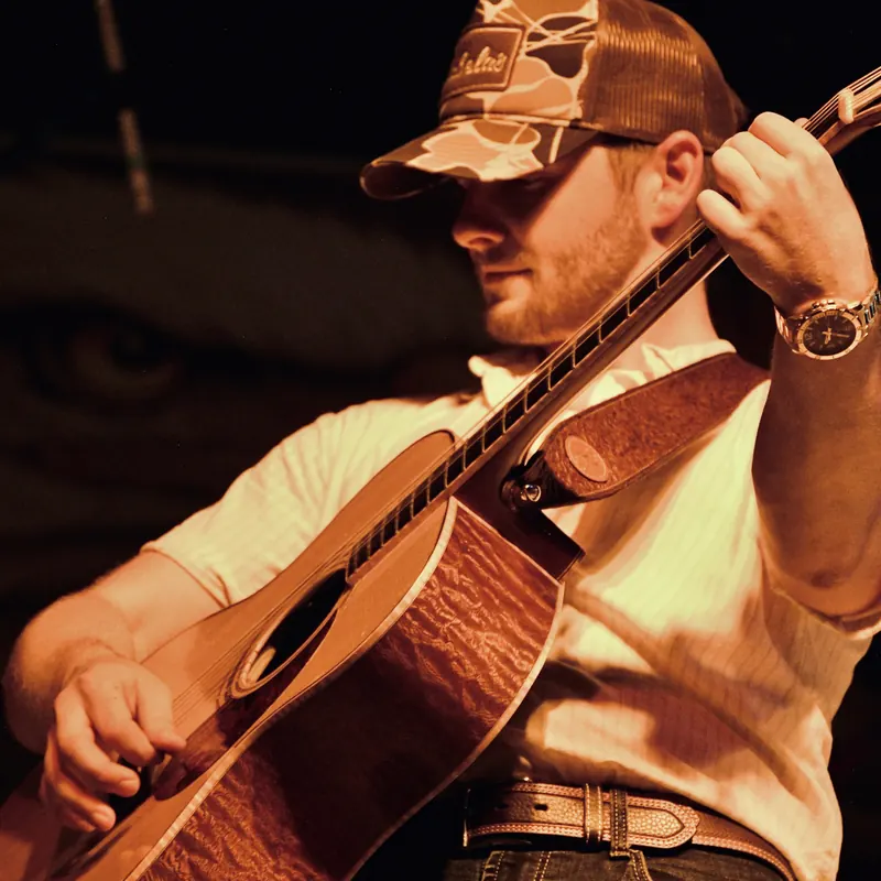Acoustic guitarist in a camo cap in warm light