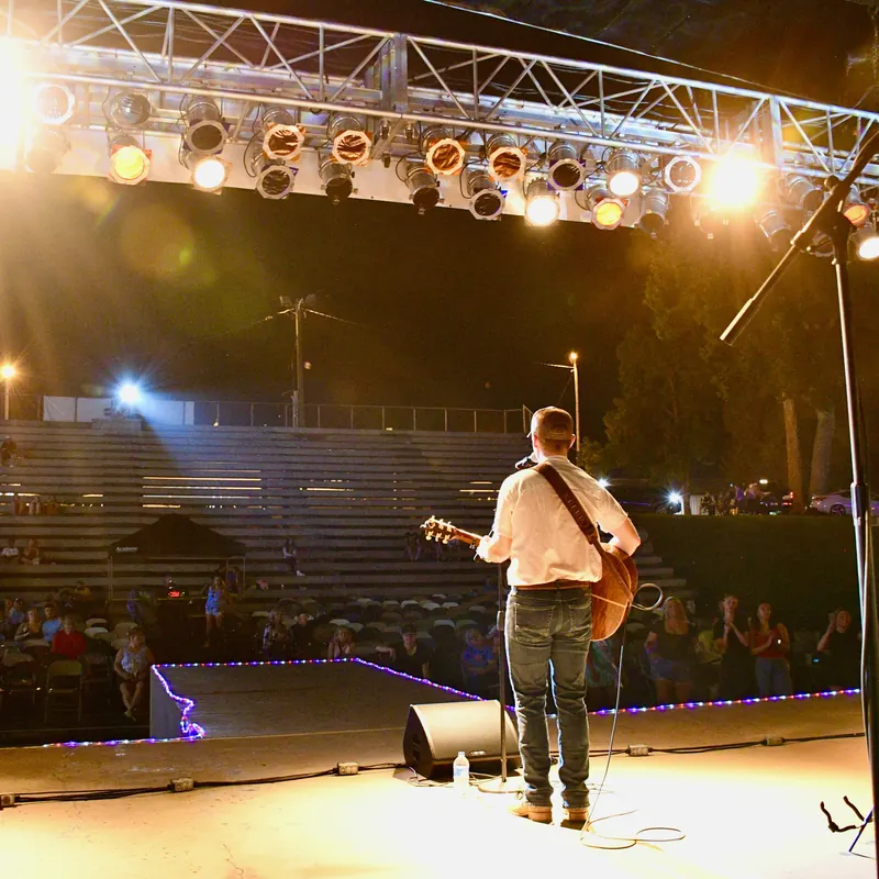 Wide view of the festival stage under truss lights, bleachers beyond