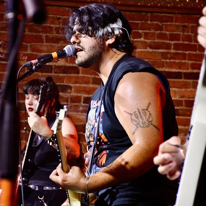 Singer at the microphone in front of a brick wall, guitarist behind
